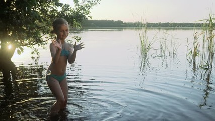 Cute little girl is catching soap bubbles standing in the water of a picturesque forest lake. Slow motion.