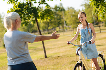 Obraz premium Cheerful little girl approaching her grandmother on the bicycle