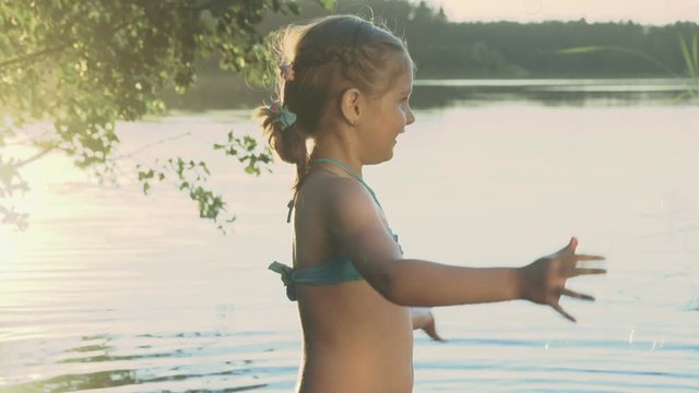 Cute little girl is catching soap bubbles standing in the water of a picturesque forest lake close-up. Slow motion.