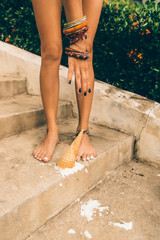 Close up of tragedy, bad day, negative emotions. Woman drop ice cream cone on her feet on the stone stairs in tropical house resort and want to lift it up. Outdoor lifestyle on hot sunny summer day.