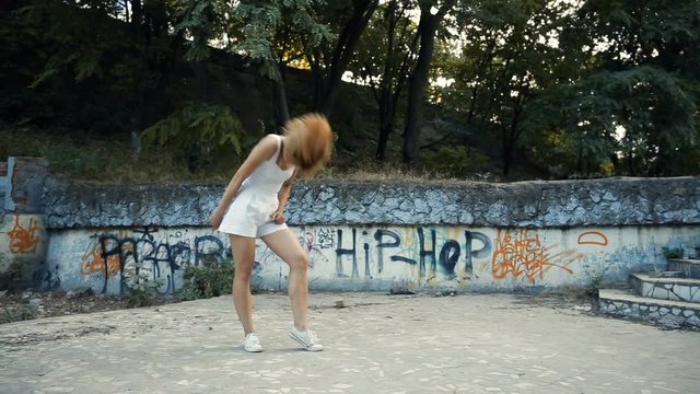 Young Asian woman dancing modern choreography in city park, outside. City ruins and graffiti. Direction is jazz-funk, hip-hop.
