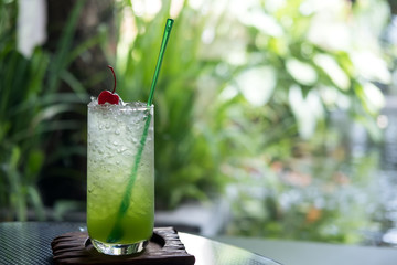 A glass of kiwi italian soda on a wooden saucer in cafe with green nature background