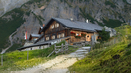 Fototapeta na wymiar Panoramic view in the Alps with traditional mountain hut and fresh green mountain pastures on a sunny day, Austria.