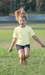 little girl making exercising with skipping rope at stadium at summer day