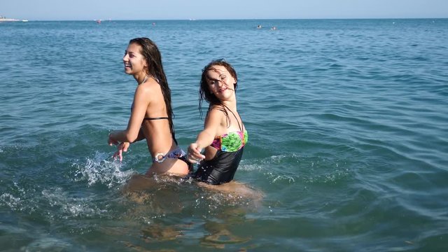 Two sexy girlfriends, brunette and red-haired are enjoying themselves in the sea. Sprinkle each other with water and have fun. Slow motion. 4K.