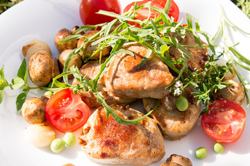 Roasted pork medallions with cherry tomato, mushrooms and arugula on white plate