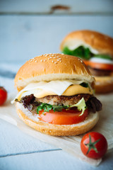 Two hamburgers with beef burger cutlet, fried onion, spinach, ketchup sauce and blue cheese in traditional buns, served on wood chopping board over bright turquoise background. Copy space
