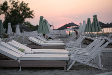 White beach beds, chairs and umbrellas on sunset; selective focus background.
