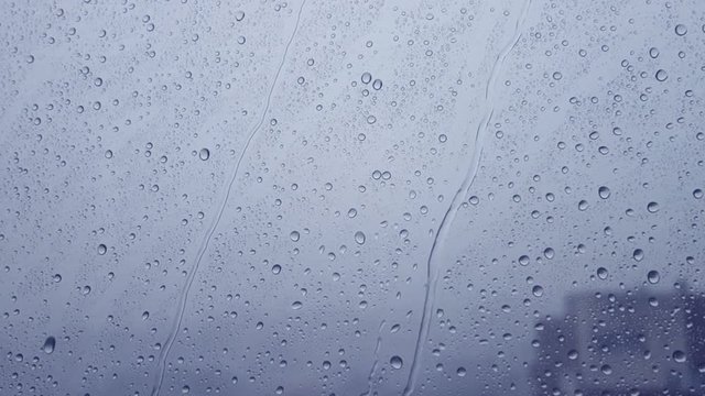 Storm Rain drops running down on a window pane. Blue tint.