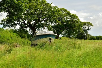 Abandoned cabin cruiser boat in a field viewed from face on.