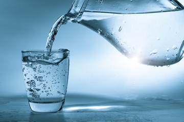 Drinking water is poured into a glass from a jug