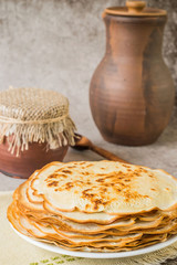  Home meal. Traditional Russian pancakes, clay pot with sour cream and a jug of milk on an old gray background.