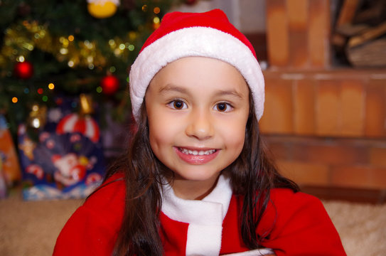Beautiful smiling litle girl wearing a christmas clothes with a christmas tree background with some presents