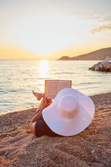Woman reading a book on the beach at sunset