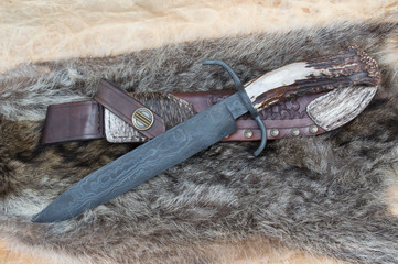 A big bowie knife with leather sheath displayed on top of a coon skin