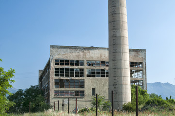 Abandoned and crumbling vintage obsolete industrial building with chimney in front of it