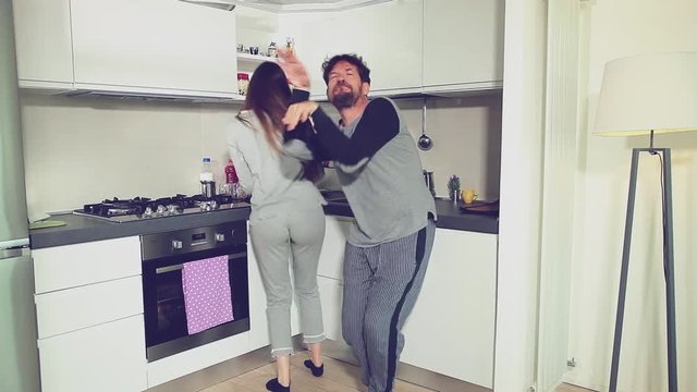 Cute couple dancing and eating donuts in kitchen in pajamas wide shot