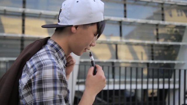 Young Man Walking On The Street And Smoke E-Cigarette. Vape.