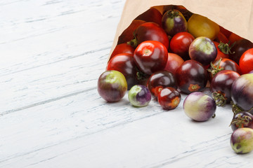 Different tomatoes in the paper bag on the white wooden background