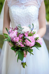 The bride holds a wedding bouquet of peonies closeup