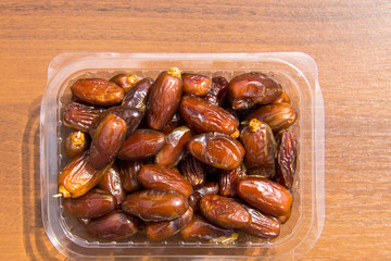 Dried date fruits in plastic container on wooden table. Top view