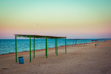 Abandoned beach at sunset. Sandy coast with old aged tents and umbrellas, blue wavy  water and colorful sky.