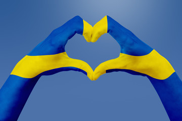 Hands flag of Sweden, shape a heart. Concept of country symbol, on blue sky.