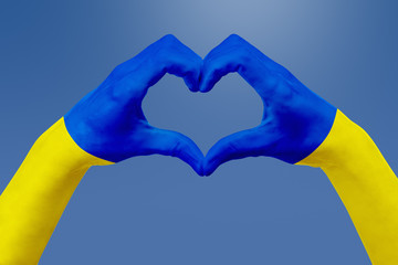 Hands flag of Ukraine, shape a heart. Concept of country symbol, on blue sky.