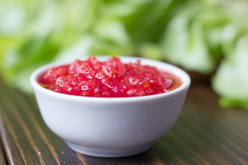 Mexican salsa or indian chutney in white ceramic bowl against green herbs