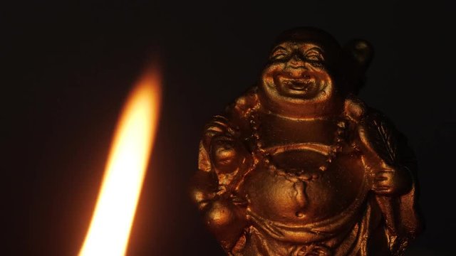 Buddha statue in the darkness being it by a candle. Closeup shot.