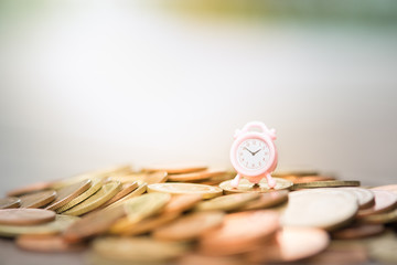 Miniature alarm clock with coins under gold sun light.Saving money.Financial report.Time is money and wealth.Passive income concept.