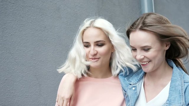 Hipster young adult friends embracing while hanging out in the city. Two young women laughing and walking enjoying carefree vacation lifestyle