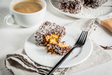 Australian food. Traditional dessert Lamington - pieces of biscuit in dark chocolate, sprinkled with coconut powder chips. On a marble plate, white table. With coffee mug. Copy space