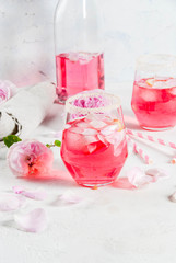 Summer refreshment drinks. Light pink rose cocktail, with rose wine, tea rose petals, lemon. On a white stone concrete table. With striped pink tubules, petals and rose flowers. Copy space