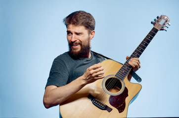 Obraz premium A man with a beard on a blue background holds a guitar, music, musical instruments, play, strings