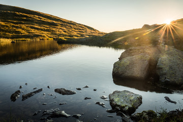 Sonnenaufgang über einem See mit Steine im Vordergrund