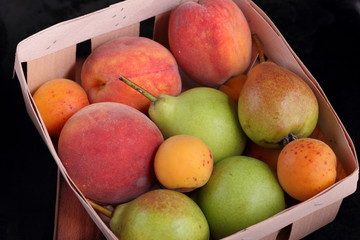 Pears, peaches and apricots in a basket on a dark background