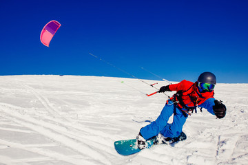Snowboarder with a kite on fresh snow in the winter in the tundra of Russia against a clear blue...