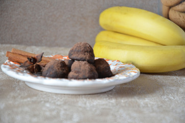 Chocolate truffles of candy on a plate, with cinnamon and anise. On a serviced table with bananas