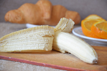 Half peeled Banana, Open Banana On a cutting board , Slices of orange and croissant on the background