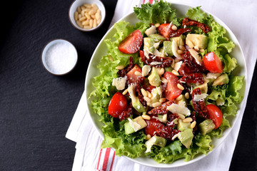Salad from lettuce, cherry tomatoes, dried tomatoes, avocado, parmesan, pine nuts with olive oil. Healthy food.