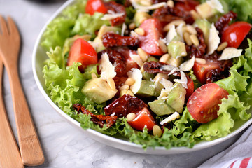 Salad from lettuce, cherry tomatoes, dried tomatoes, avocado, parmesan, pine nuts with olive oil. Healthy food.