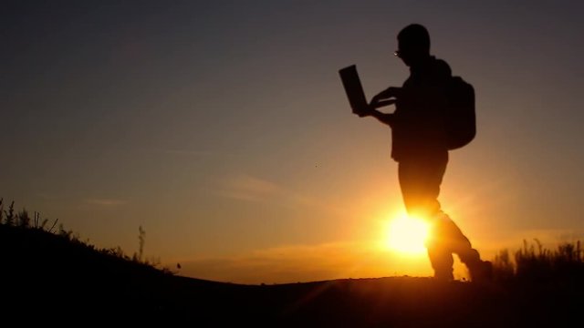 Silhouette of business man with laptop working on the field at sunset time. Concept freelancer, performing tasks, anger from failure and throwing a laptop.