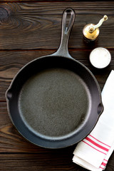 Cast-iron frying pan with salt and pepper on a wooden background.