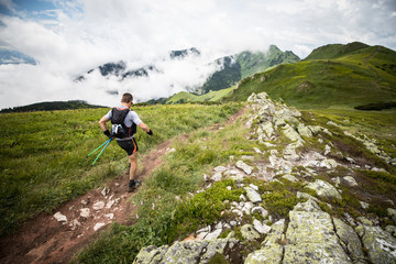 middle age male runner with backpack and poles on the mountain trail after rain with cloudy view