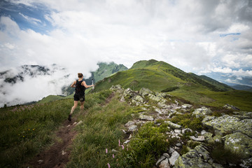 female runner running fast on technical ridge trail in the green mountains with beautiful scenery and view