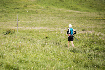 Naklejka na ściany i meble ultra race runner with poles and backpack running alone on mountain alpine meadow trail
