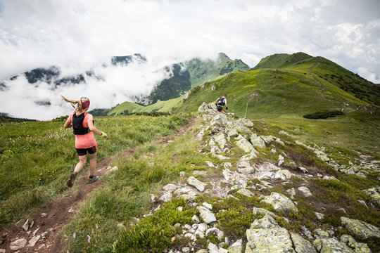 young woman with long hair running fast down the hill on mountain trail with beautiful mountain