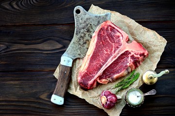 Raw t-bone steak with garlic and rosemary on an old wooden background. Rustic style.