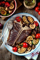 Grilled t-bone steak with grilled vegetables on an old wooden background. Rustic style.